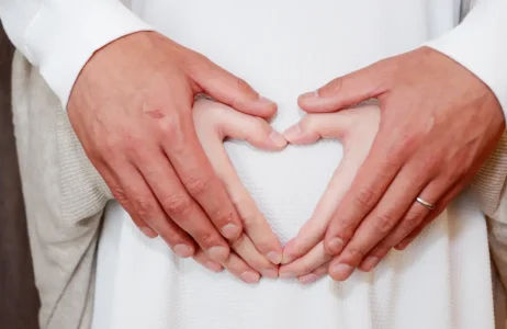 Manos de pareja en embarazo formando un corazon